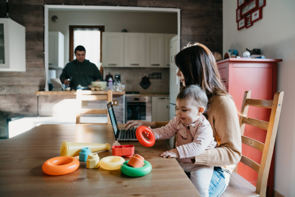 Woman using a laptop while holding a baby on her lap